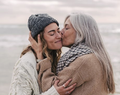 Two women, one older and one younger, embracing each other on a beach.